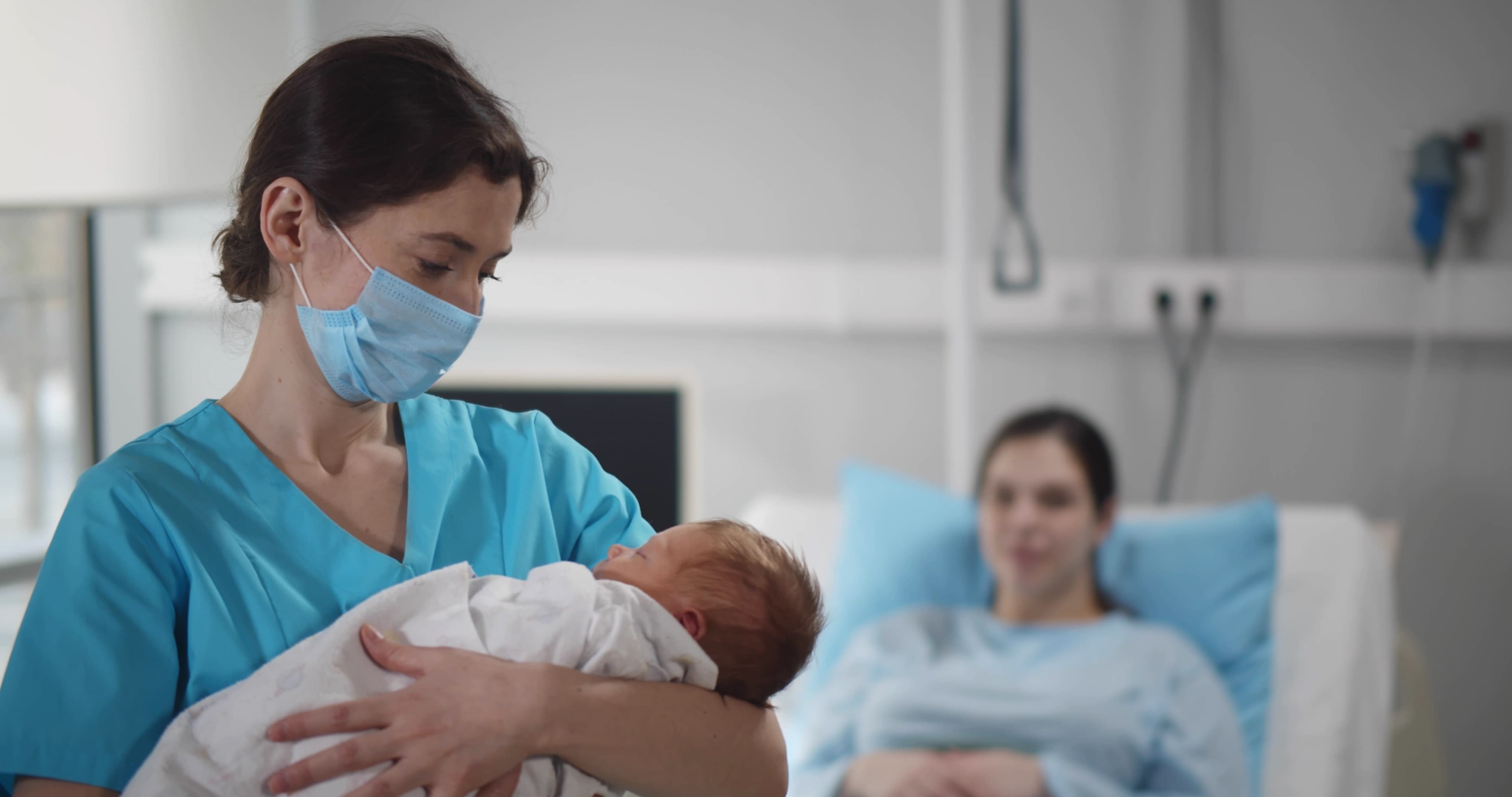 Labor and delivery nurse holding newborn with mother in background