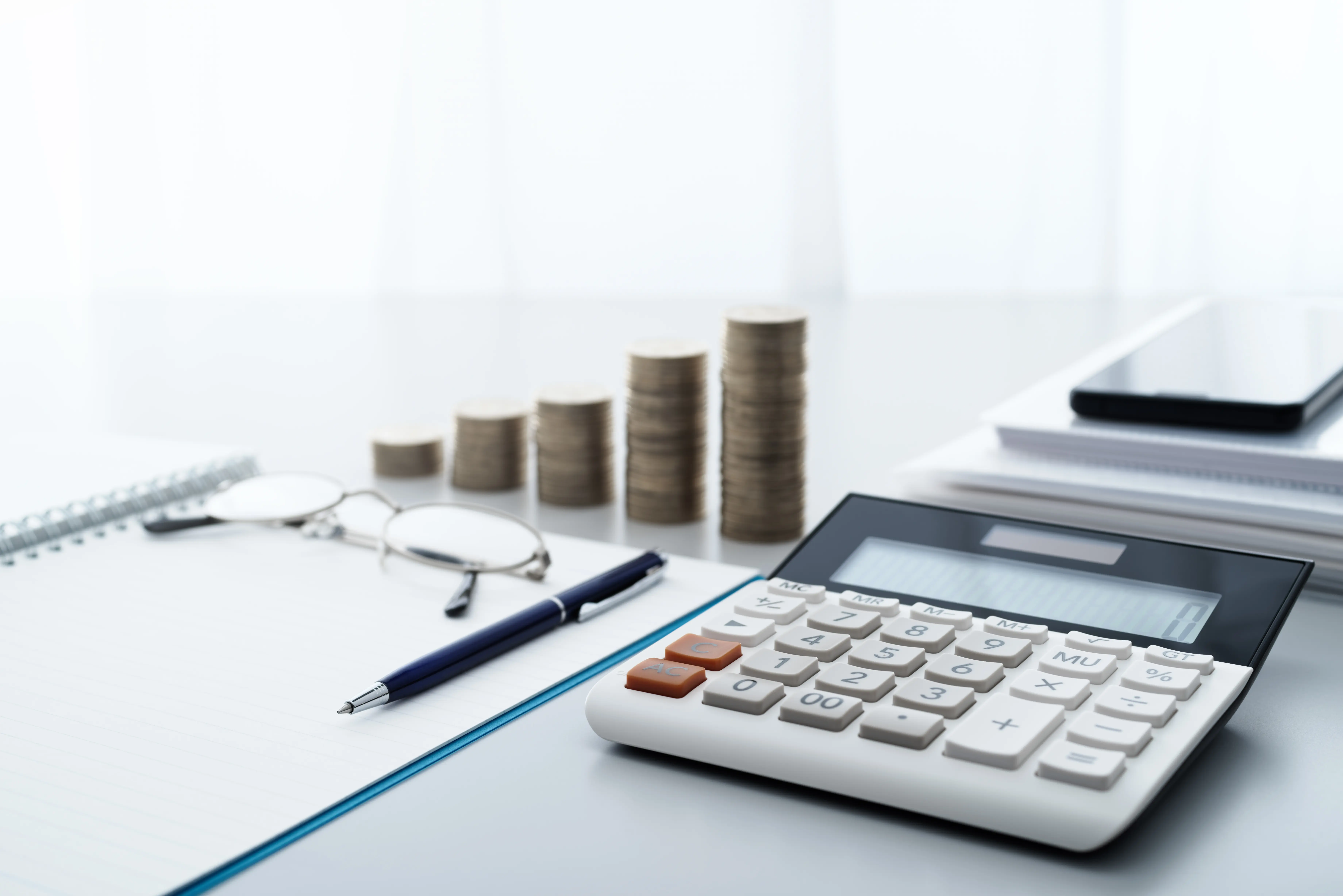 A calculator, notepad and stack of coins